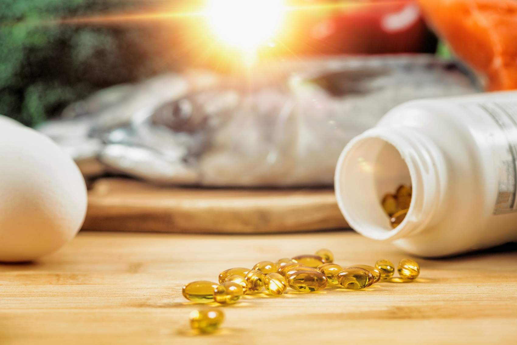 Supplement Bottle with Gel Capsules On a Wooden Table. Natural Food Sources of Vitamin D In Background.