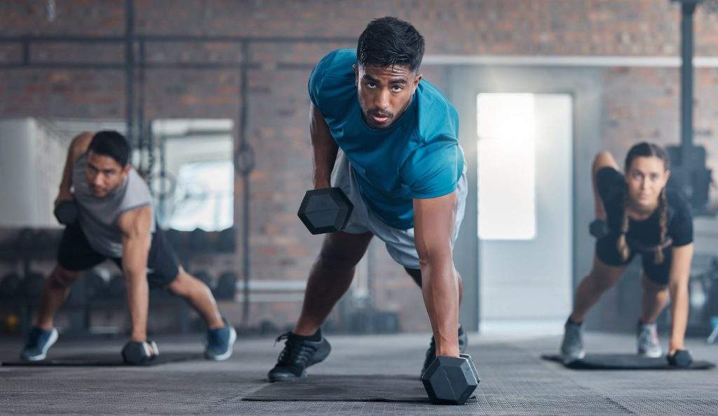 Men, woman and dumbbells in gym workout, training and exercise for strong body muscles, health and wellness. Portrait, sweat or fitness weightlifting class for people or friends with personal trainer.